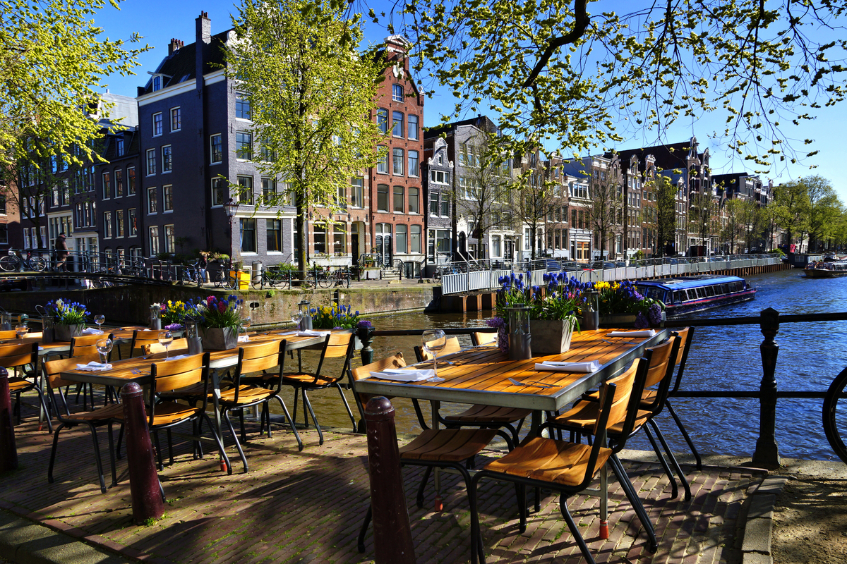 Restauranttische entlang der wunderschönen Grachten von Amsterdam unter blauem Himmel im Frühling