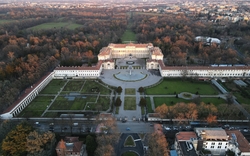 Luftaufnahme eines großen, symmetrischen Palastes umgeben von Gärten und Straßen.