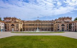 Historisches Gebäude mit Brunnen im Vordergrund und blauem Himmel.
